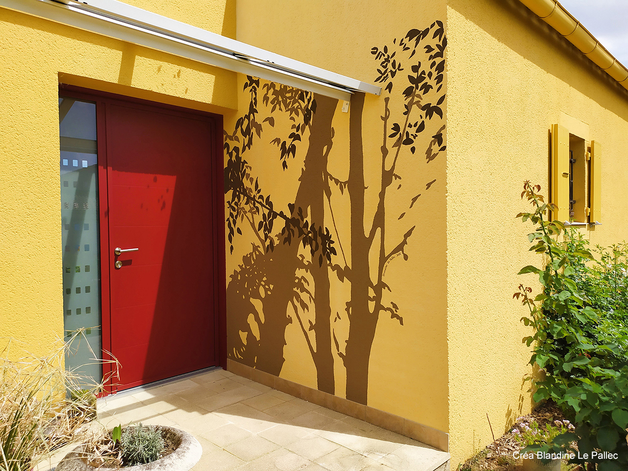 Peinture murale extérieure, réalisée prés de la porte d'entrée d'une maison, représentant un jeu d'ombres d'arbre. Couleur terre d'ombre er brun sur mur jaune.